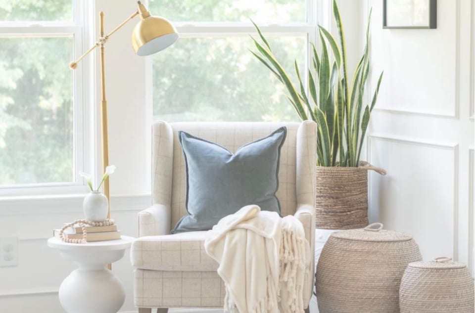A sunlit armchair with a blue pillow, a throw and plants