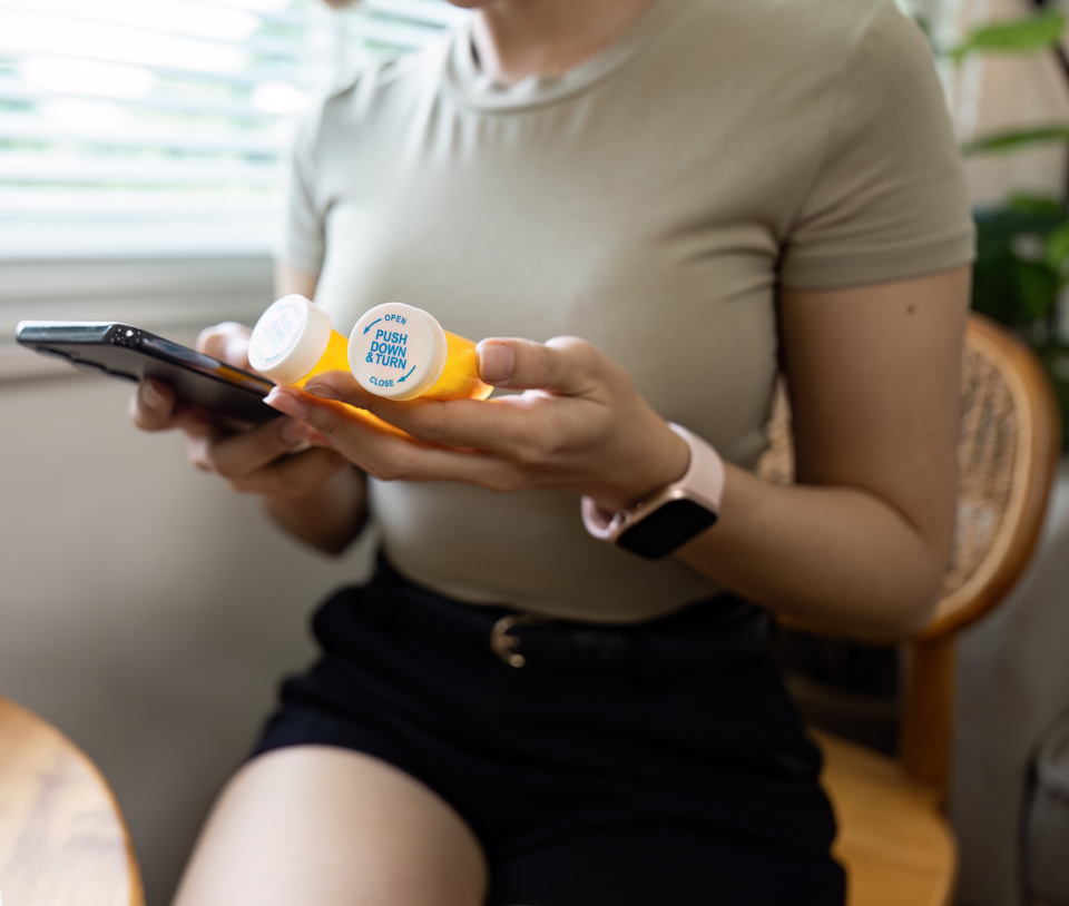 A woman reading a medicine bottle with her phone in hand